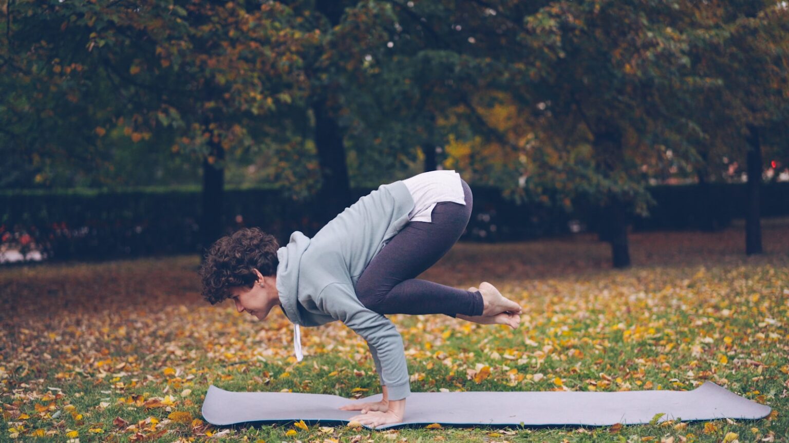 Person practicing yoga crow pose on mat outdoors